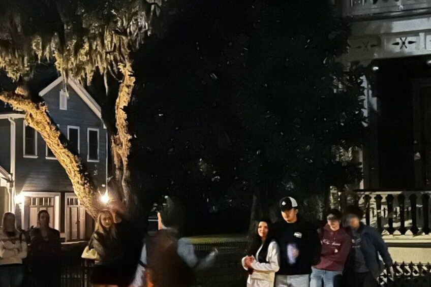A group of people gathered outdoors at night, with a house and trees in the background. 5