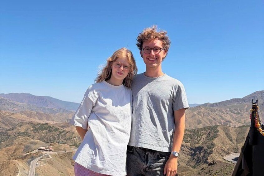Two people standing on a mountain with a clear sky and a valley in the background. 5
