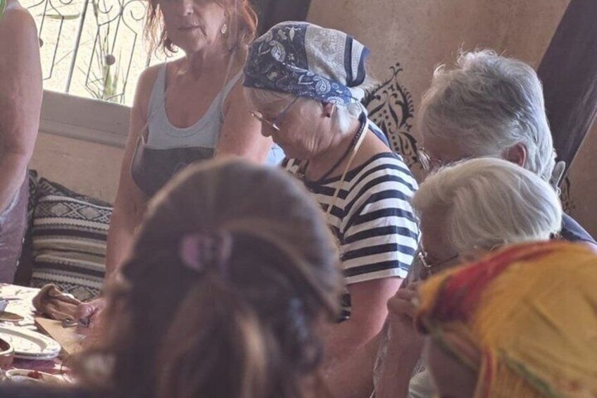 A group of people gathered indoors, some wearing bandanas, with a patterned cushion and a metal railing in the background. 4