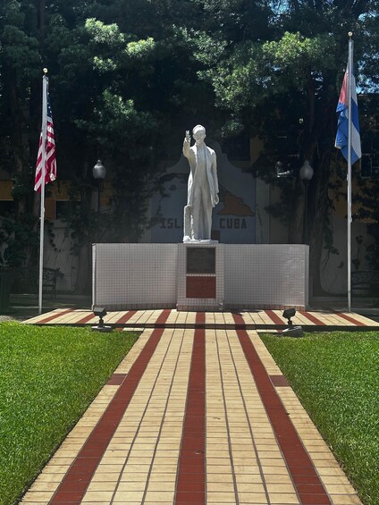 A statue of two figures on a tiled pedestal with a Cuban flag and an American flag on either side. 3