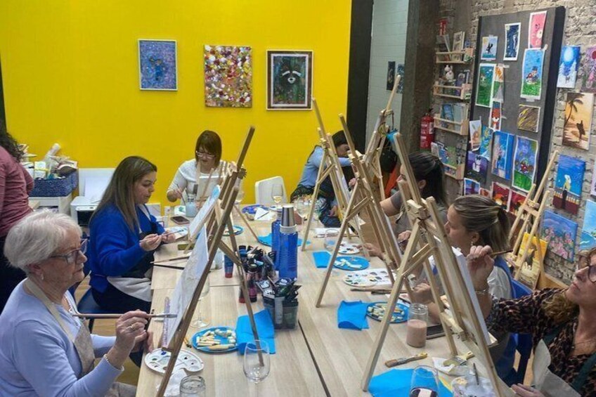 A group of people engaged in painting activities at a table with easels and art supplies. 1