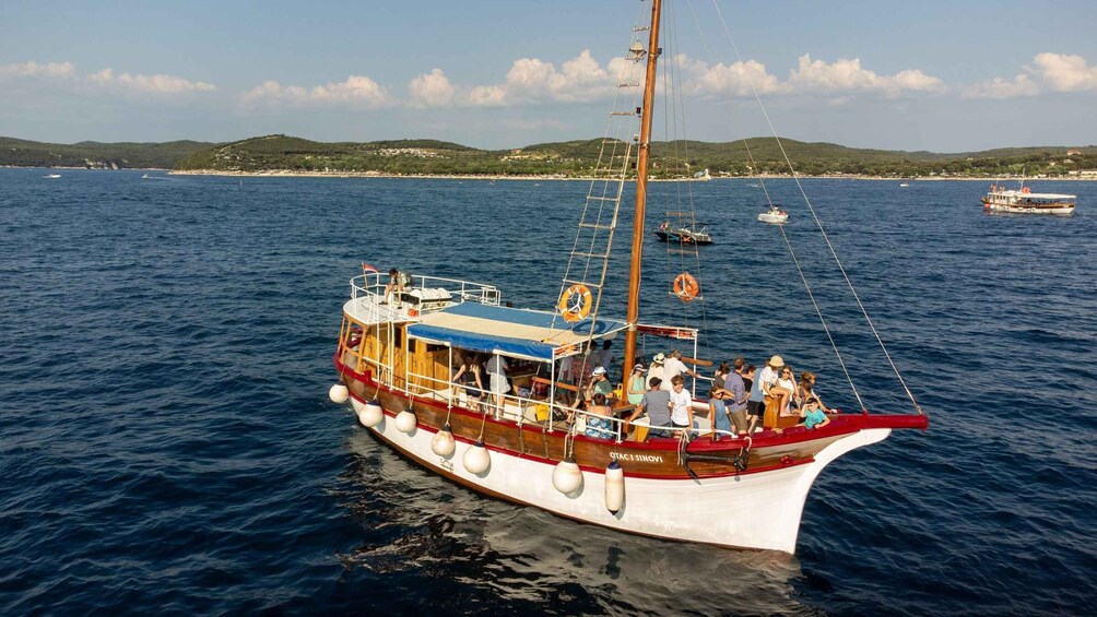 A traditional wooden boat with passengers on a calm sea, surrounded by other boats and a hilly coastline. 5