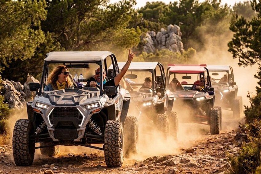 Off-road vehicles on a dusty trail surrounded by trees and rocks. 1