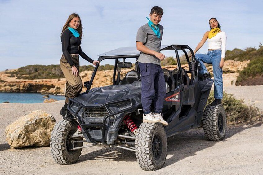 Three people standing next to a black ATV on a rocky terrain with a body of water in the background. 5