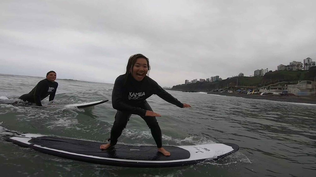 Two people surfing on a wave in the ocean with a cityscape in the background. 5