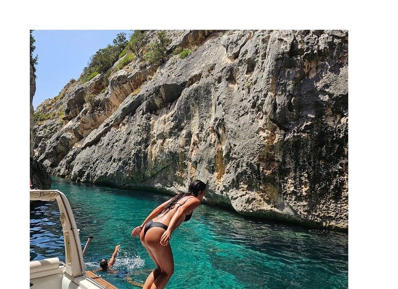 A woman in a bikini diving into clear blue water surrounded by rocky cliffs. 1