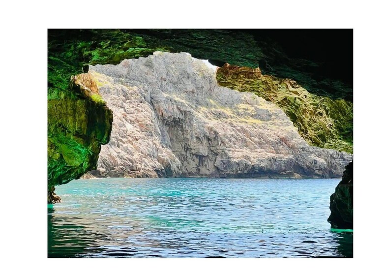 A coastal cave entrance with clear blue water and green algae-covered rocks. 3