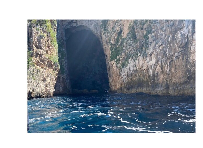 A rocky coastal cave entrance with clear blue water. 5