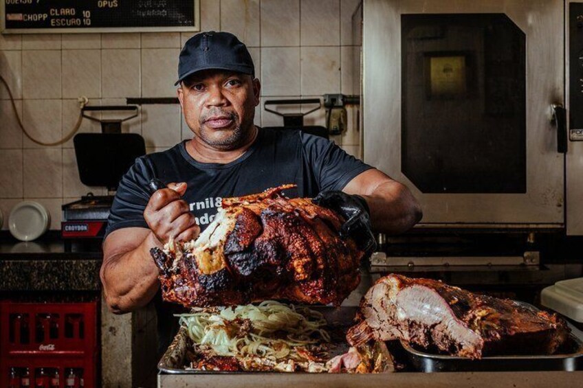 A person holding a large roasted pig in a kitchen. 5