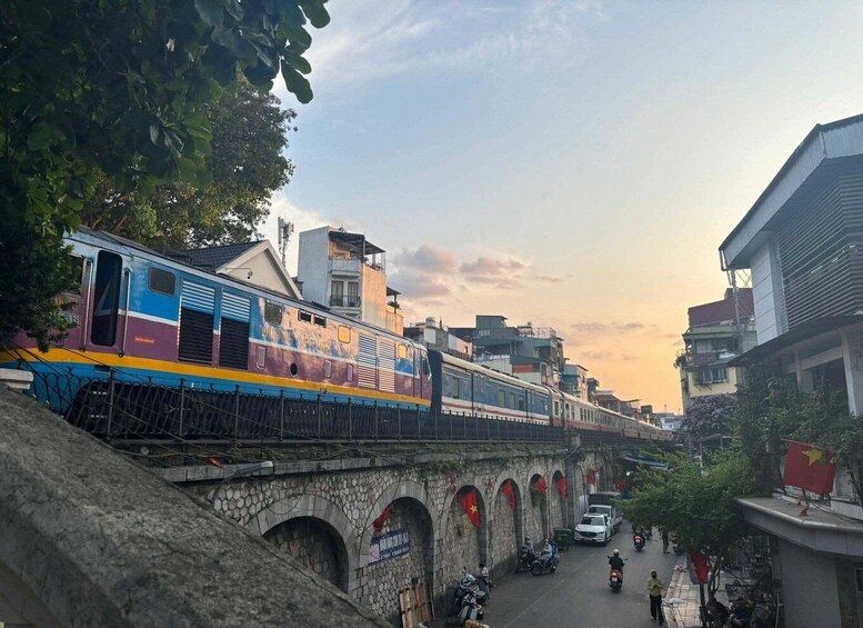 A train crossing a stone bridge with buildings and flags in the background. 2