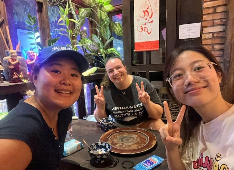 Three people sitting at a table with a bowl of food, a plate, and a smartphone. 4