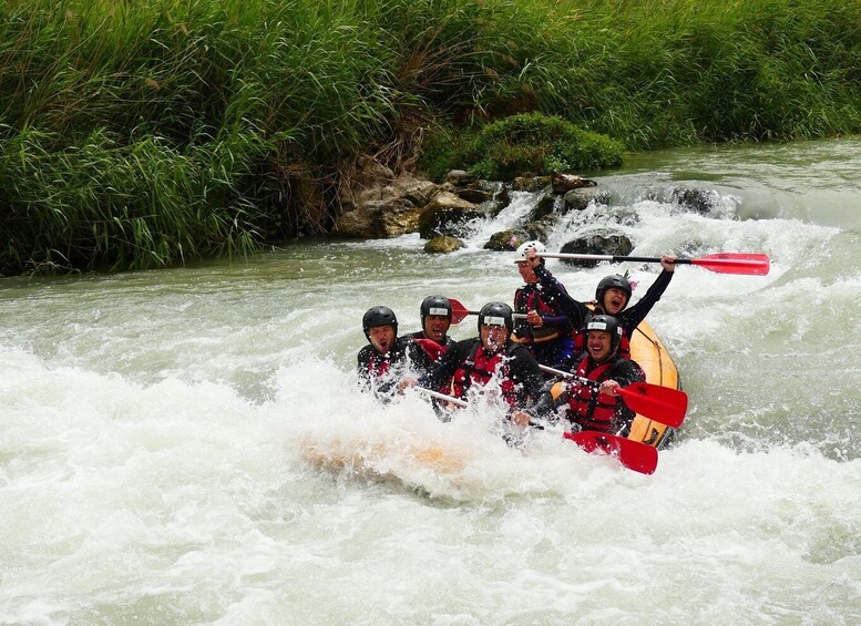 A group of people in a white raft navigating a river with rapids, surrounded by greenery. 4