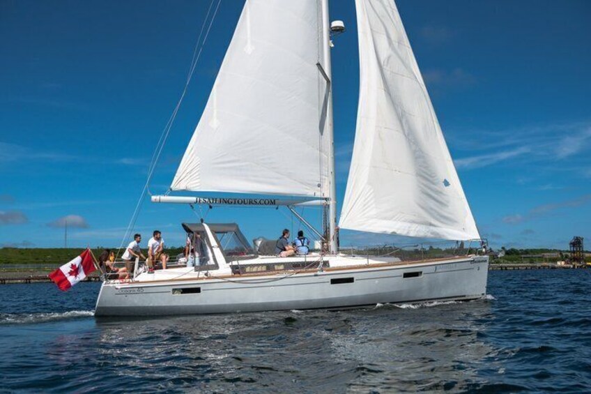 A sailboat with a Canadian flag, people on deck, and a clear blue sky. 3