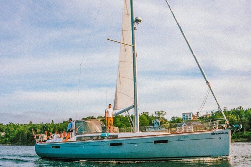 A sailboat with a crew on a calm body of water, surrounded by greenery and buildings in the background. 5
