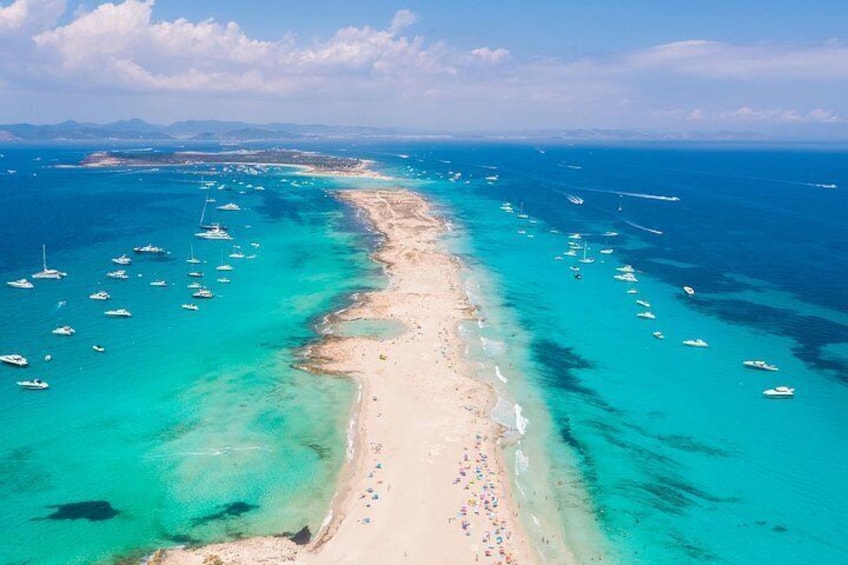 A coastal landscape with a sandy beach, clear turquoise waters, and numerous boats anchored near the shore. 1