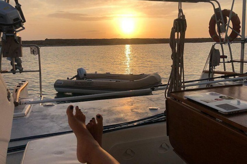 A boat with a person relaxing, a life preserver, and a sunset over water. 3