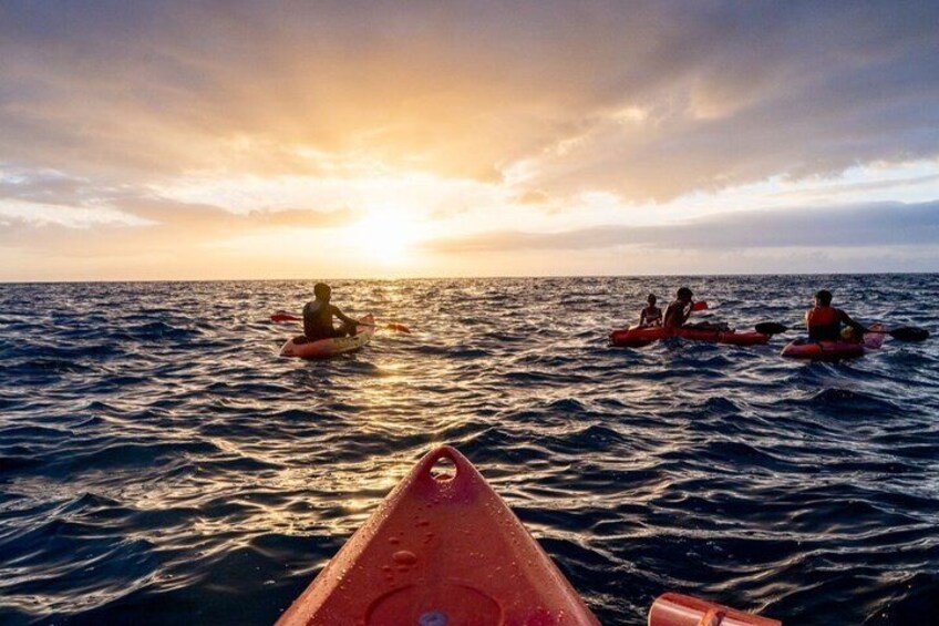 A sunset over the ocean with people in kayaks. 1