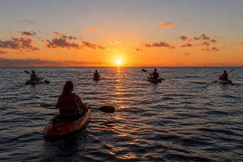 A sunset over calm waters with people kayaking. 3