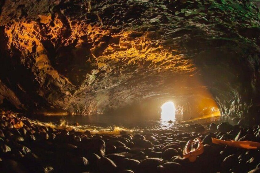 A cave with a water stream and a light source at the end of the tunnel. 2