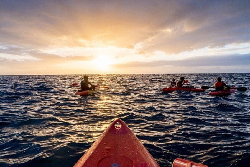 A sunset over the ocean with people kayaking. 1