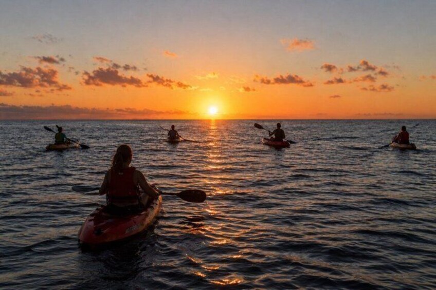 A sunset over the ocean with people kayaking. 3