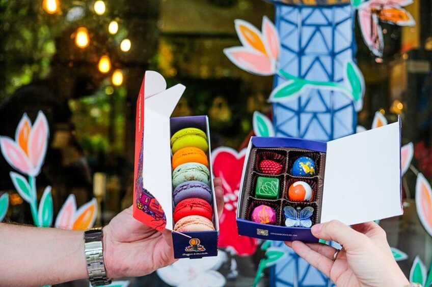 Dos manos sostienen cajas abiertas de macarons, una con macarons de colores y otra con sabores variados. 2