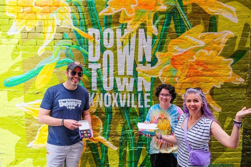 Un mural con el texto 'DOWNTOWN KNOXVILLE' y tres personas de pie frente a él. 1