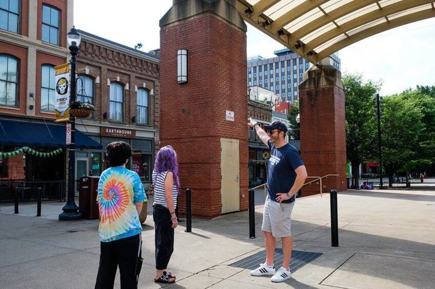 Three people standing on a sidewalk, a brick building, and a covered walkway. 3