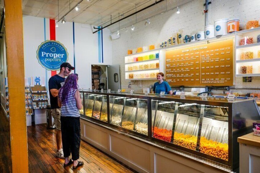 A popcorn shop interior with a display case of assorted popcorn, a menu board, and a counter where a customer is being served. 5