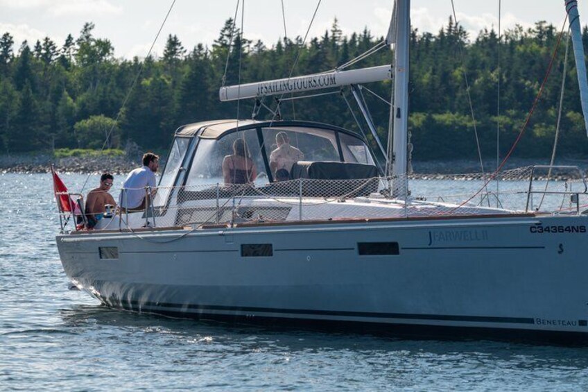 A sailboat with people on board, a flag, and a forested shoreline in the background. 3