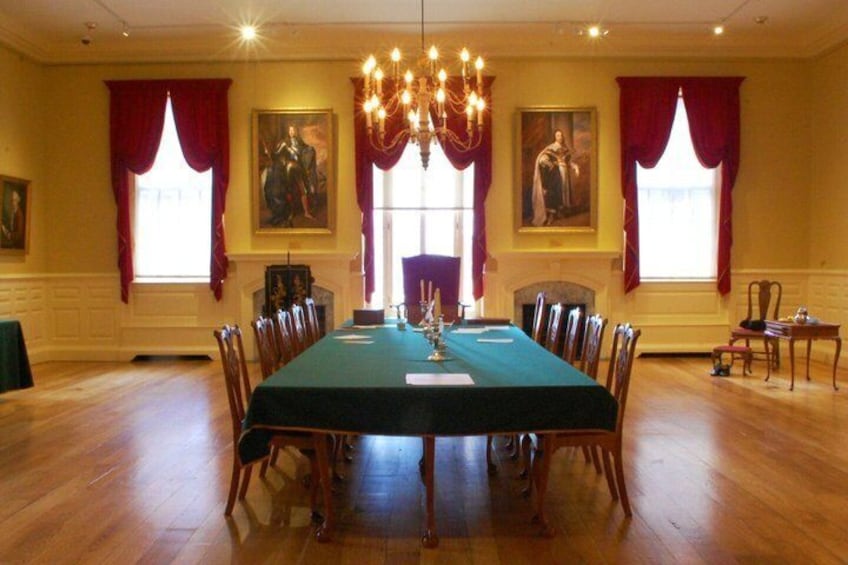 A formal dining room with a long table, chairs, a chandelier, red curtains, and paintings on the walls. 4