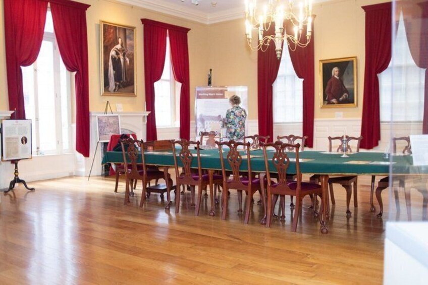A formal dining room with a long table, red curtains, and classical paintings. 2