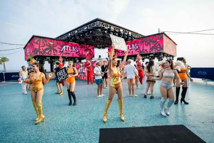 A group of people in costumes at an outdoor event with a stage and a sign that reads 'FREE SHOTTLNS.' 3