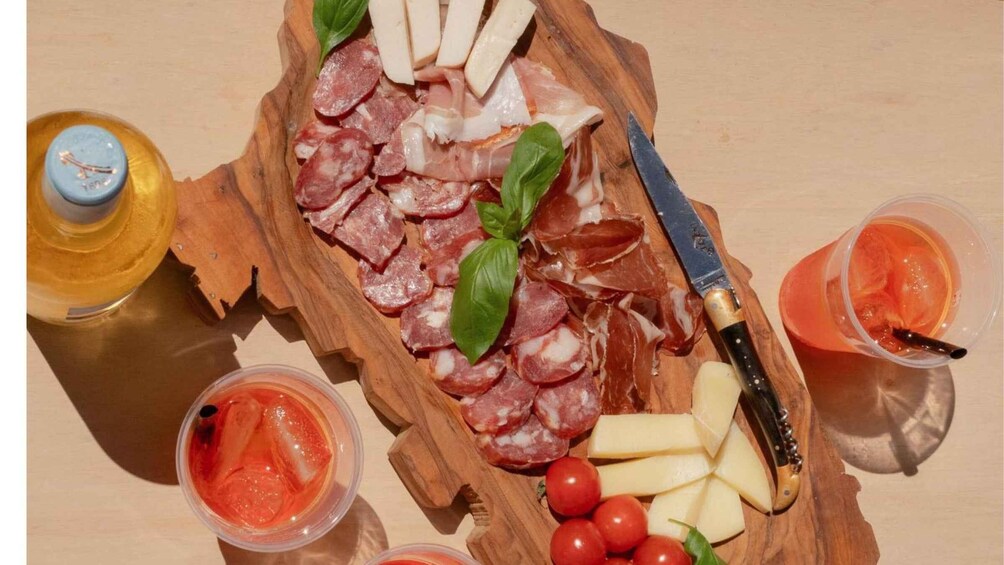 A charcuterie board with meats, cheese, tomatoes, and drinks. 2