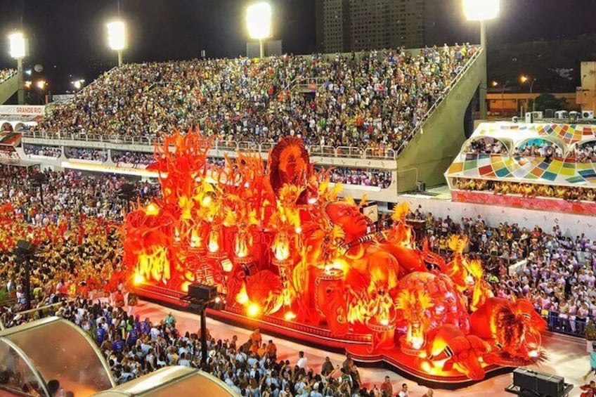 A large outdoor event with a brightly lit float featuring a dragon design. 1