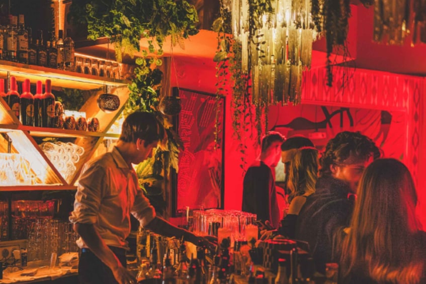 A bar with bottles and glasses, a person serving drinks, and a red-lit background. 2