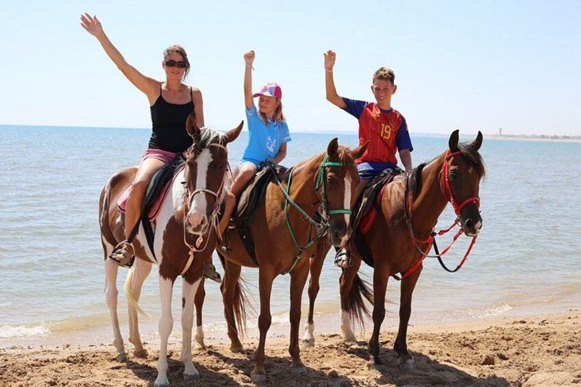 Three people riding horses on a beach with the ocean in the background. 2