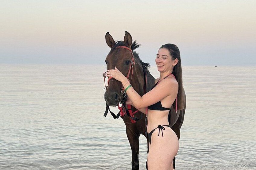A person standing by a horse near a calm body of water. 4