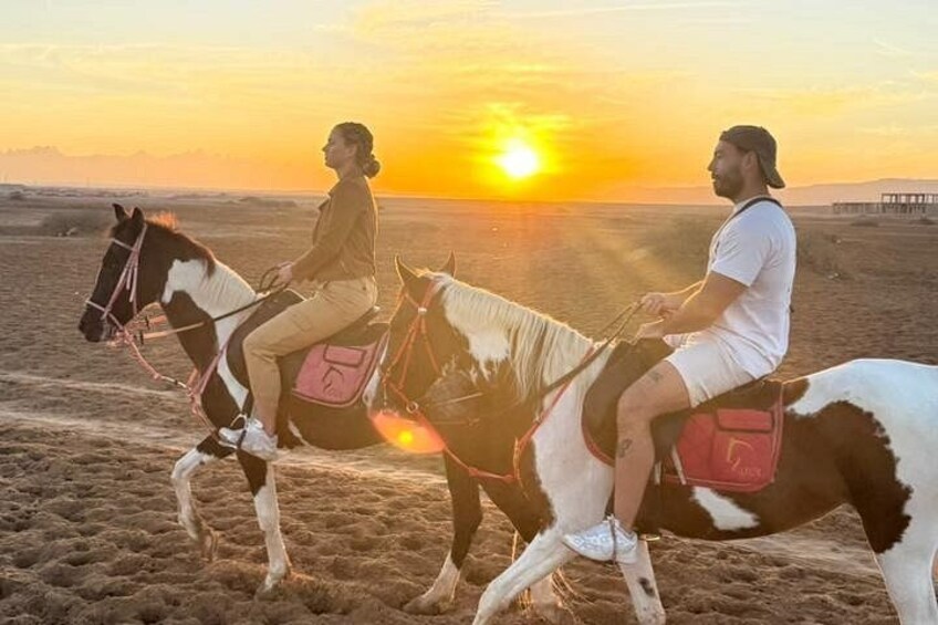 Two people riding horses on a beach at sunset. 5