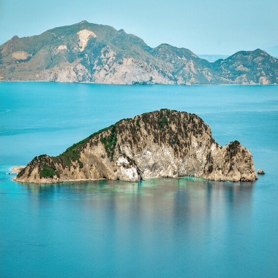A rocky island with a clear blue sea and distant mountains. 4