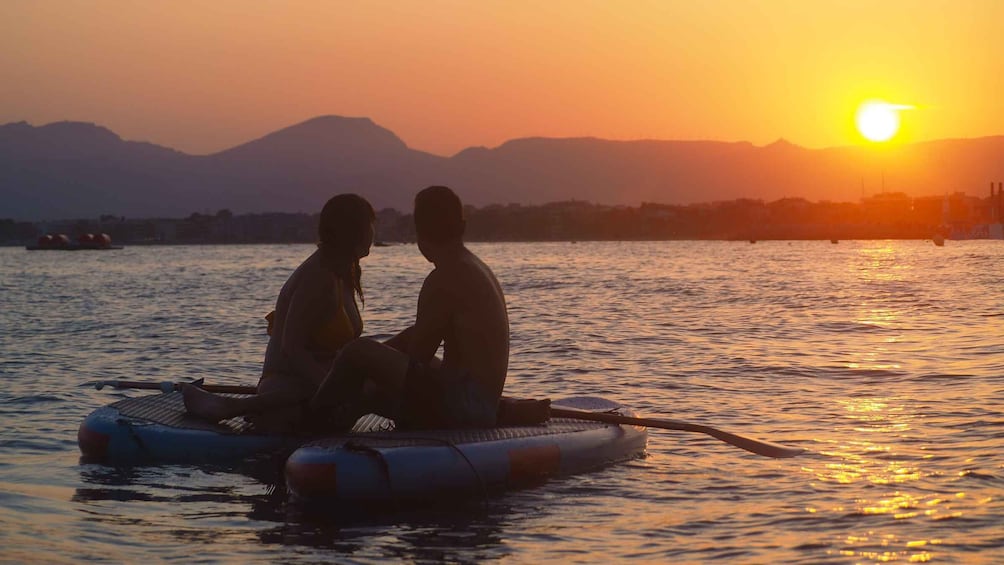Two people sitting on a raft in a body of water with a sunset in the background. 2