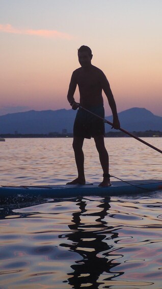 A person paddleboarding on water with mountains in the background. 5