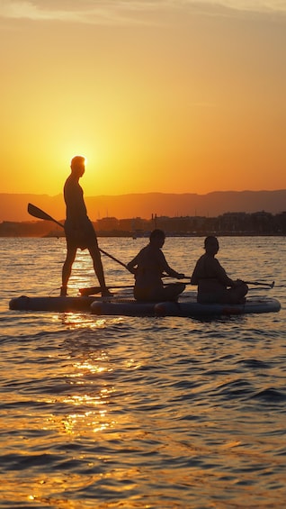 A sunset over a body of water with three people on a paddleboard. 3