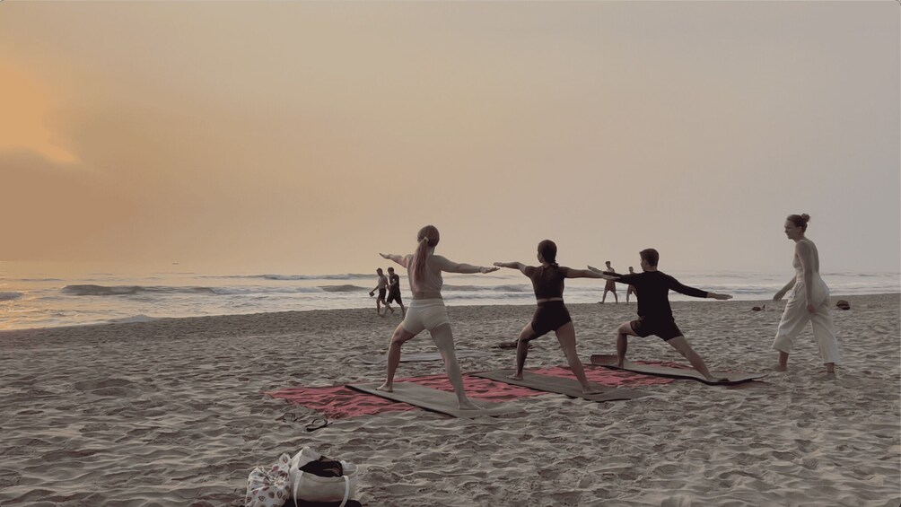 A group of people practicing yoga on mats on a beach with the ocean in the background. 2