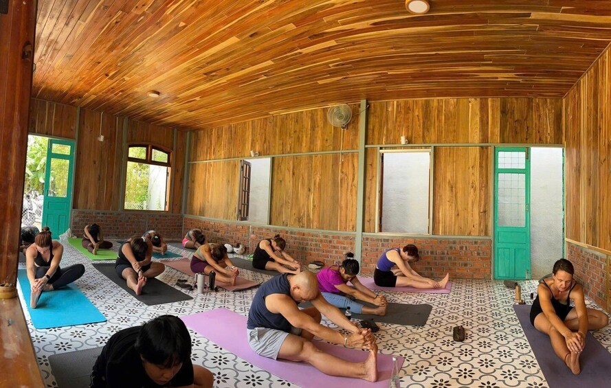 A group of people performing yoga in a wooden room with patterned floor tiles. 1