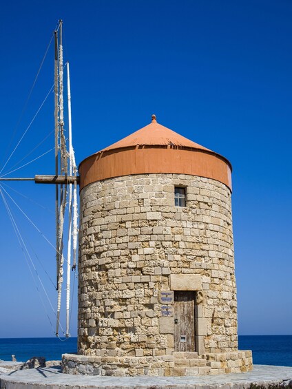 A stone tower with a red roof, a wooden door, and a large white sail structure to its left. 5