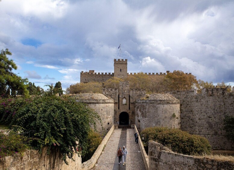 A historic stone castle with a drawbridge and a tower, surrounded by trees and a cloudy sky. 2