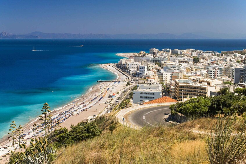 A coastal city with a beach, buildings, and a clear blue sea. 1