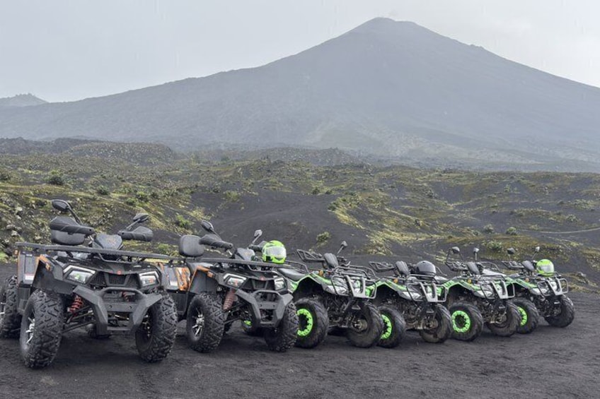 A row of quad bikes parked on a volcanic terrain with a mountain in the background. 1