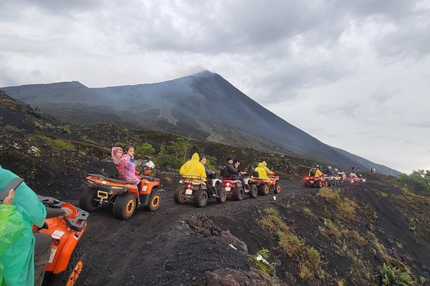 Personas conduciendo vehículos todo terreno a través de un paisaje volcánico, con una montaña al fondo. 1